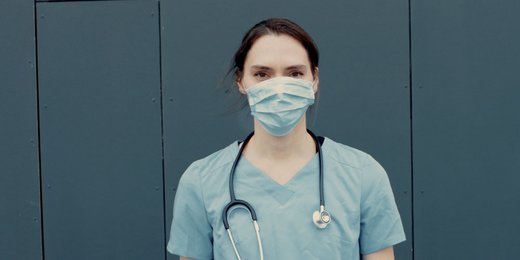 Portrait einer Krankenpflegerin mit Medizinmaske und Stethoskop, das um den Hals gelegt wurde.